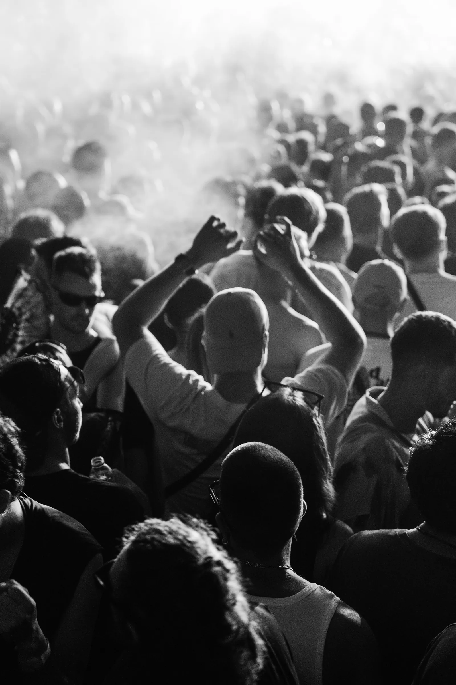 A festival crowd with hands in the air, photographed in black and white with haze in the background