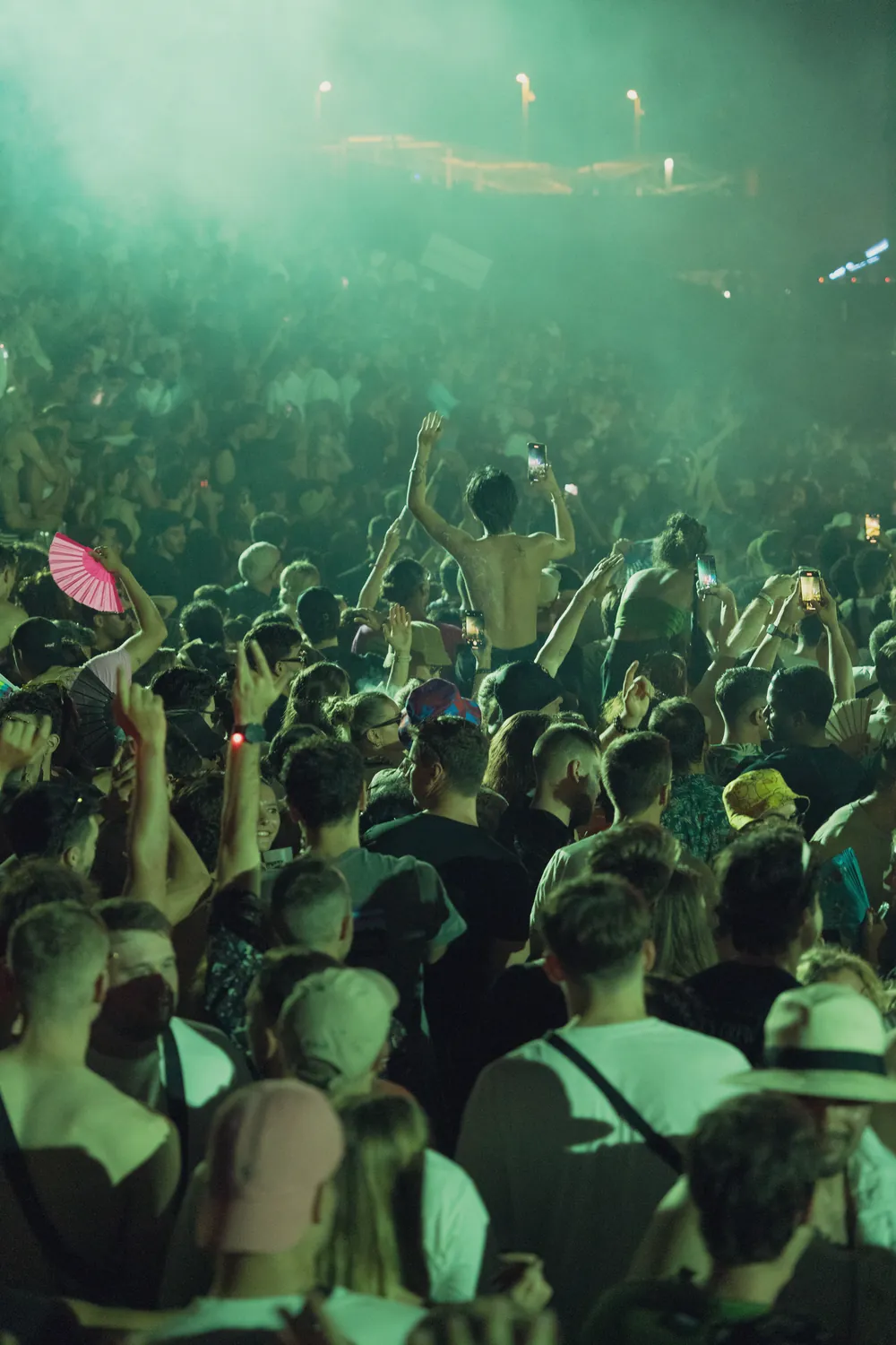 A packed festival crowd at night with raised hands under green stage light