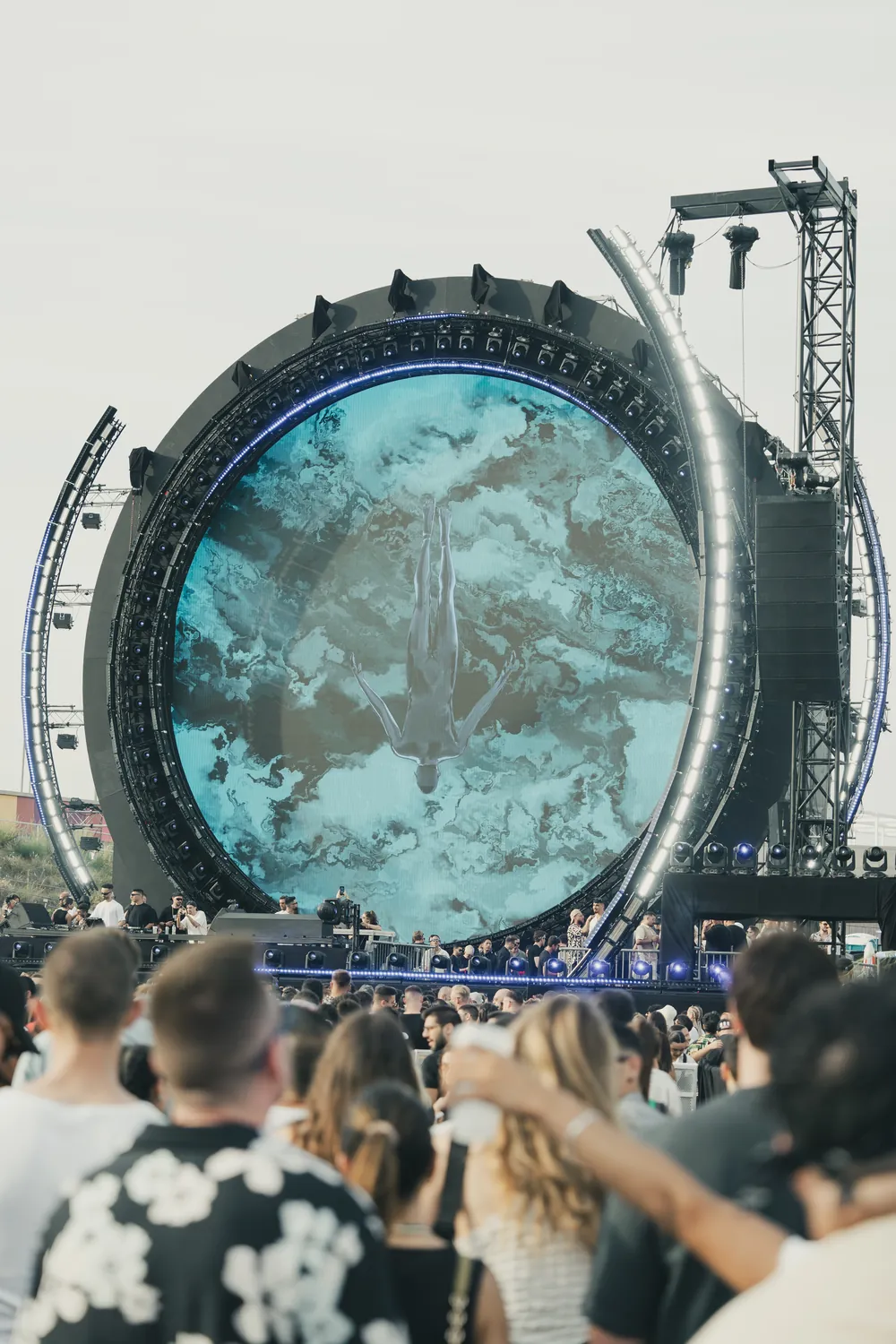 A giant circular LED stage showing an underwater image above a festival crowd in daylight